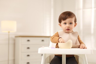 Photo of Cute little baby eating healthy food from bowl in high chair at home, space for text