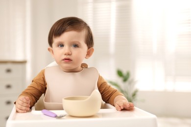 Photo of Cute little kid eating healthy baby food from bowl in high chair at home