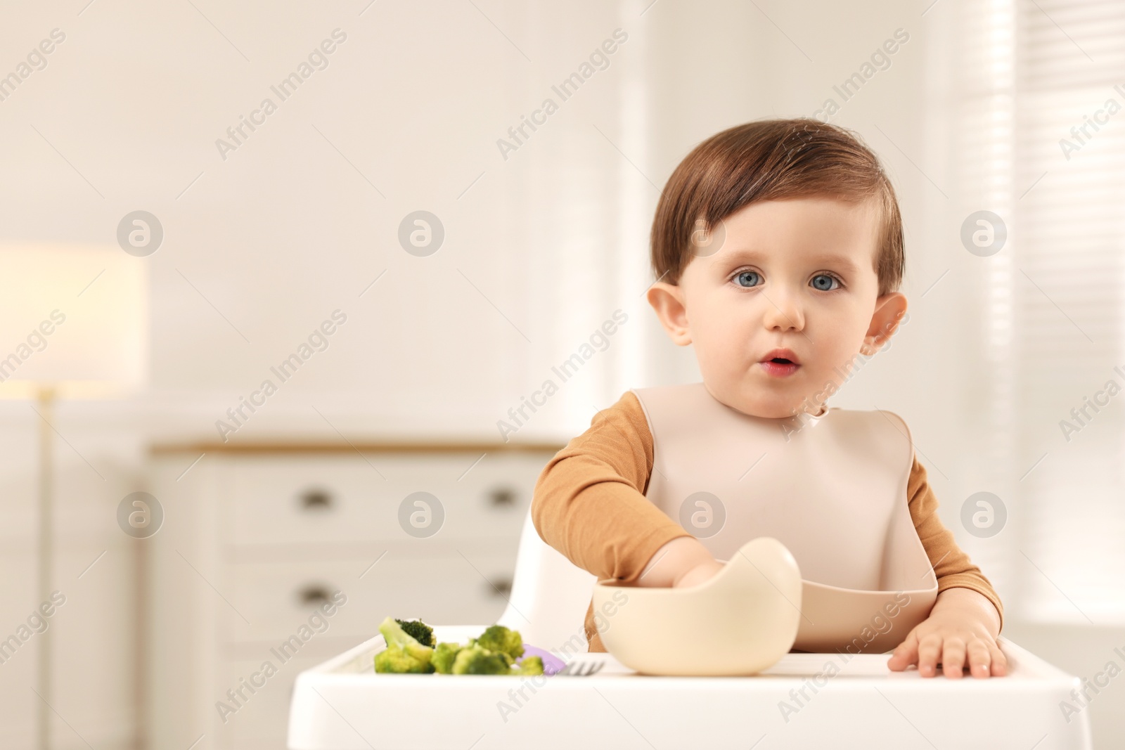 Photo of Cute little baby eating healthy food from bowl in high chair at home, space for text