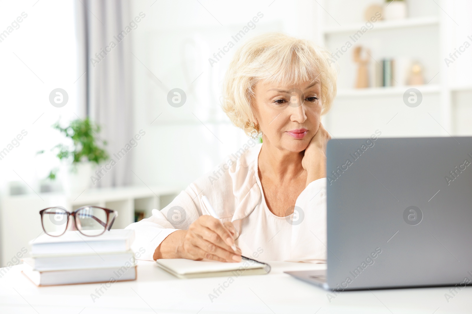 Photo of Beautiful senior woman using laptop at white table indoors