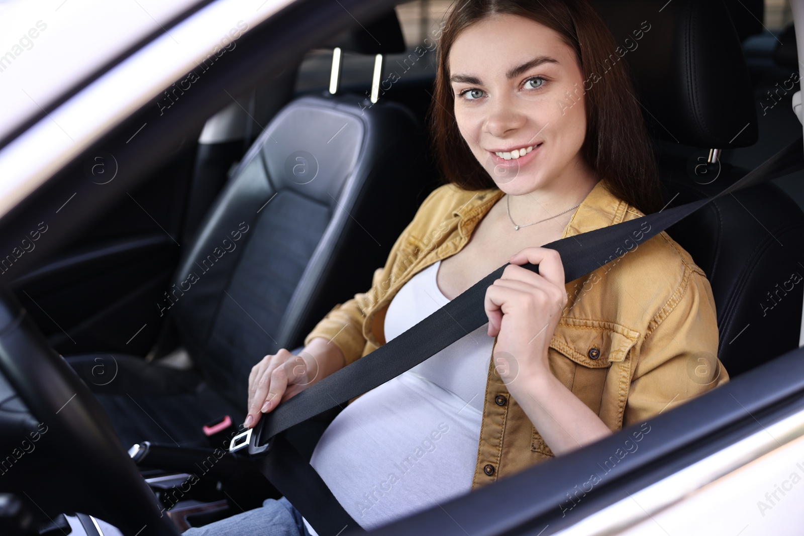 Photo of Smiling pregnant woman fastening safety belt in car, view from outside