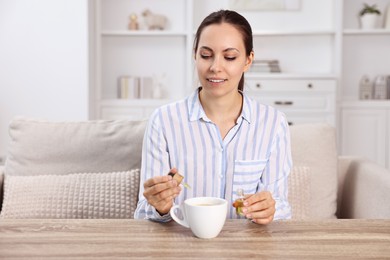 Photo of Young woman putting CBD tincture into cup with drink at wooden table