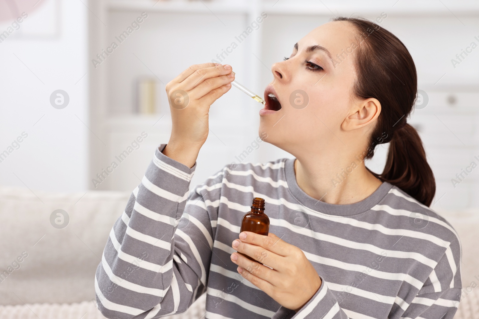 Photo of Young woman taking CBD tincture indoors. Herbal extract