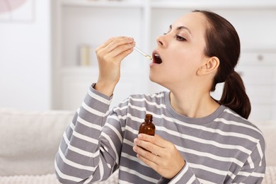 Photo of Young woman taking CBD tincture indoors. Herbal extract