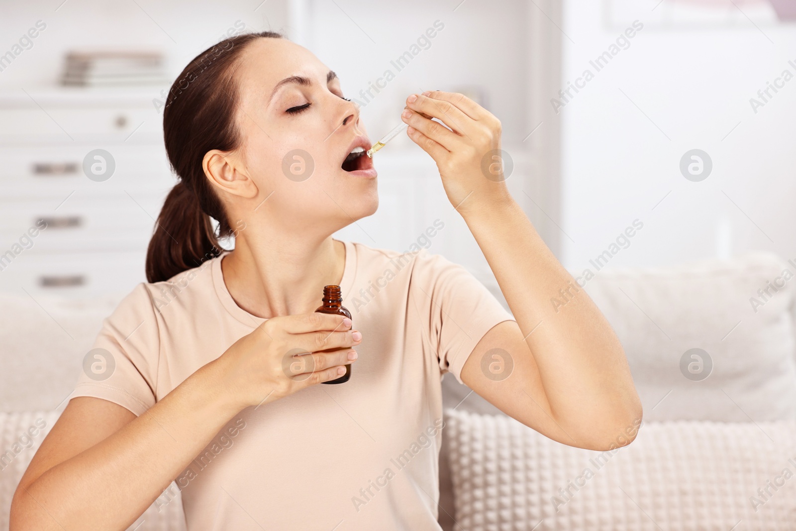 Photo of Young woman taking CBD tincture indoors. Herbal extract