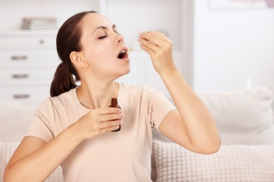 Photo of Young woman taking CBD tincture indoors. Herbal extract