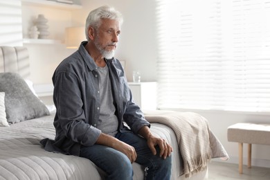 Photo of Lonely senior man sitting on bed at home