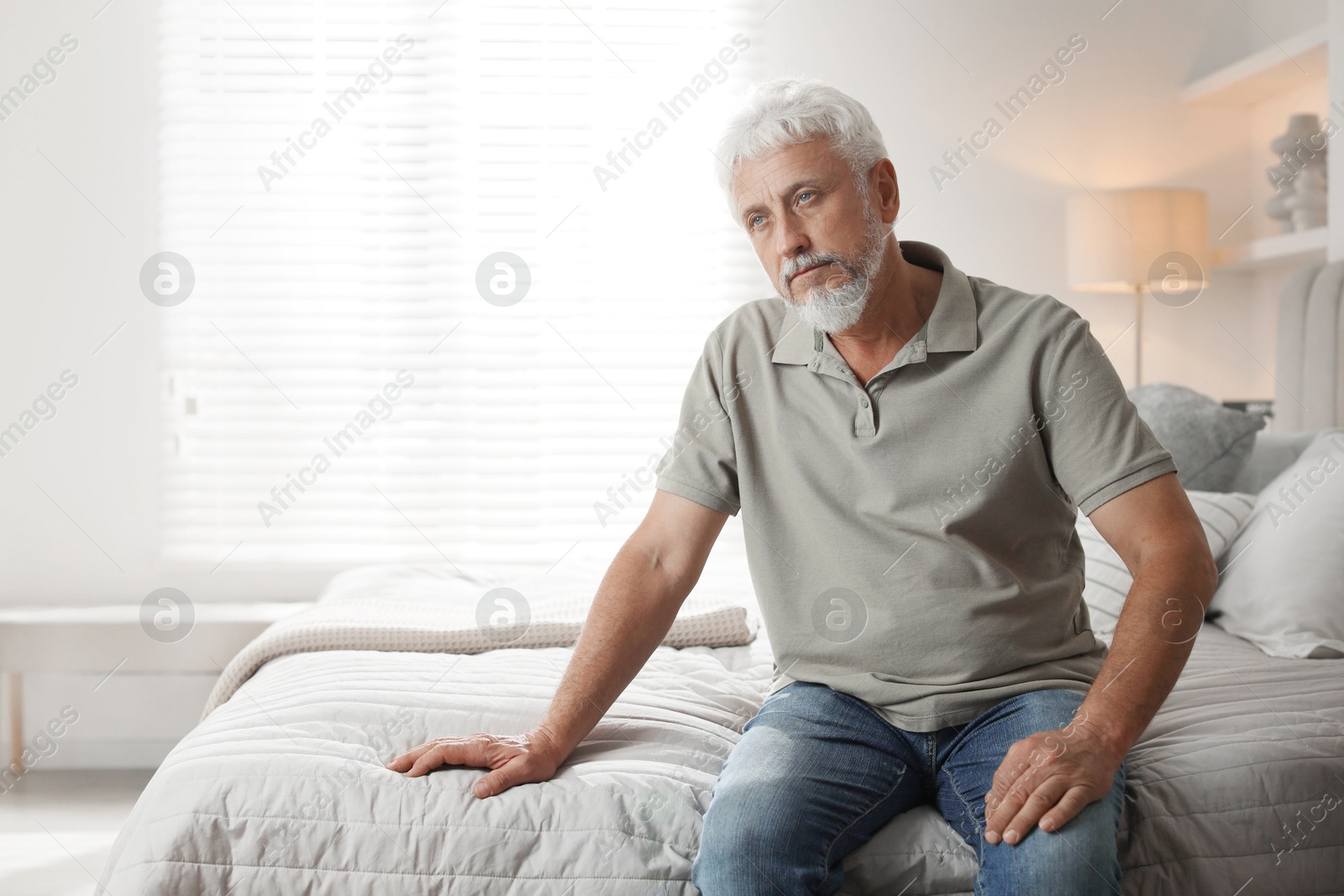 Photo of Lonely senior man sitting on bed at home. Space for text