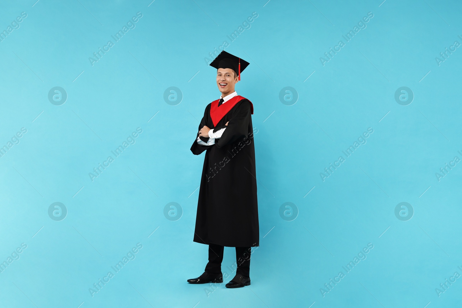 Photo of Happy student with crossed arms after graduation on light blue background