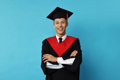 Photo of Happy student with crossed arms after graduation on light blue background