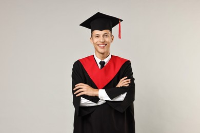 Photo of Happy student with crossed arms after graduation on grey background