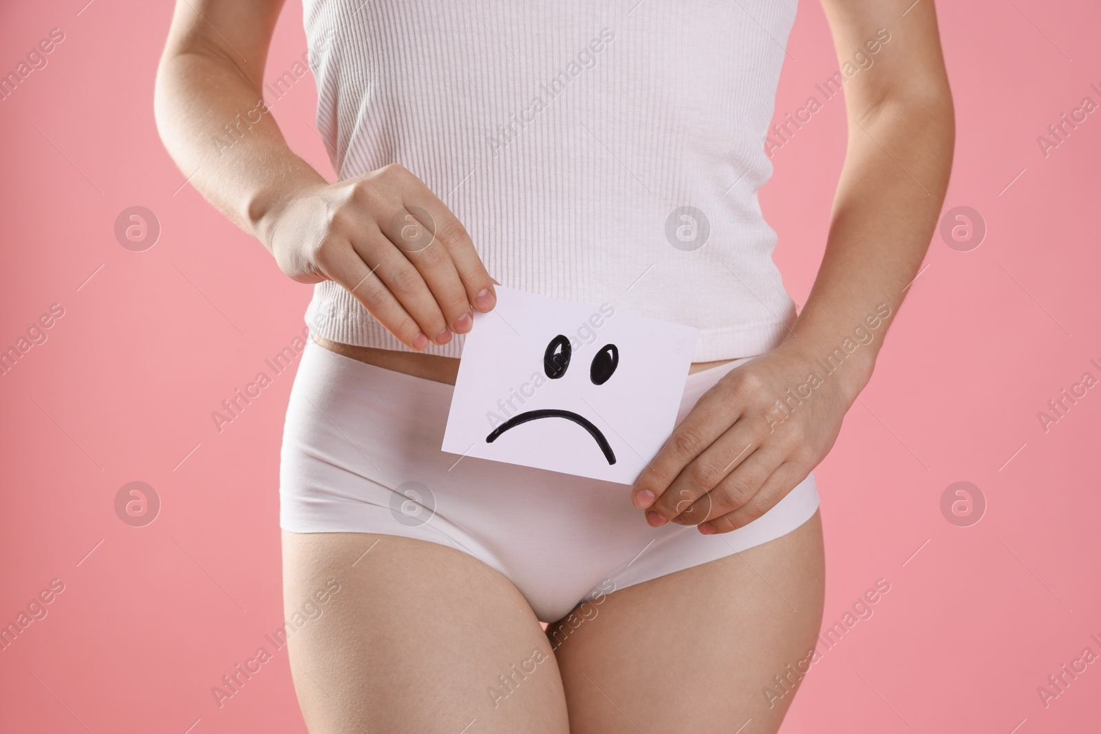 Photo of STD (sexually transmitted disease). Woman holding sticky note with drawn sad face on pink background, closeup