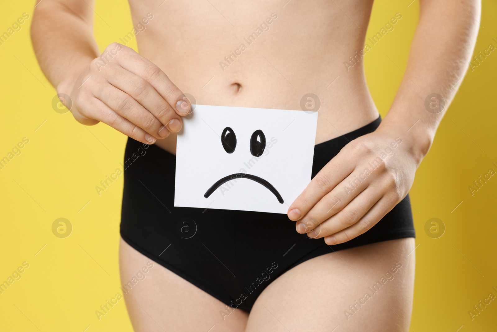 Photo of STD (sexually transmitted disease). Woman holding sticky note with drawn sad face on yellow background, closeup