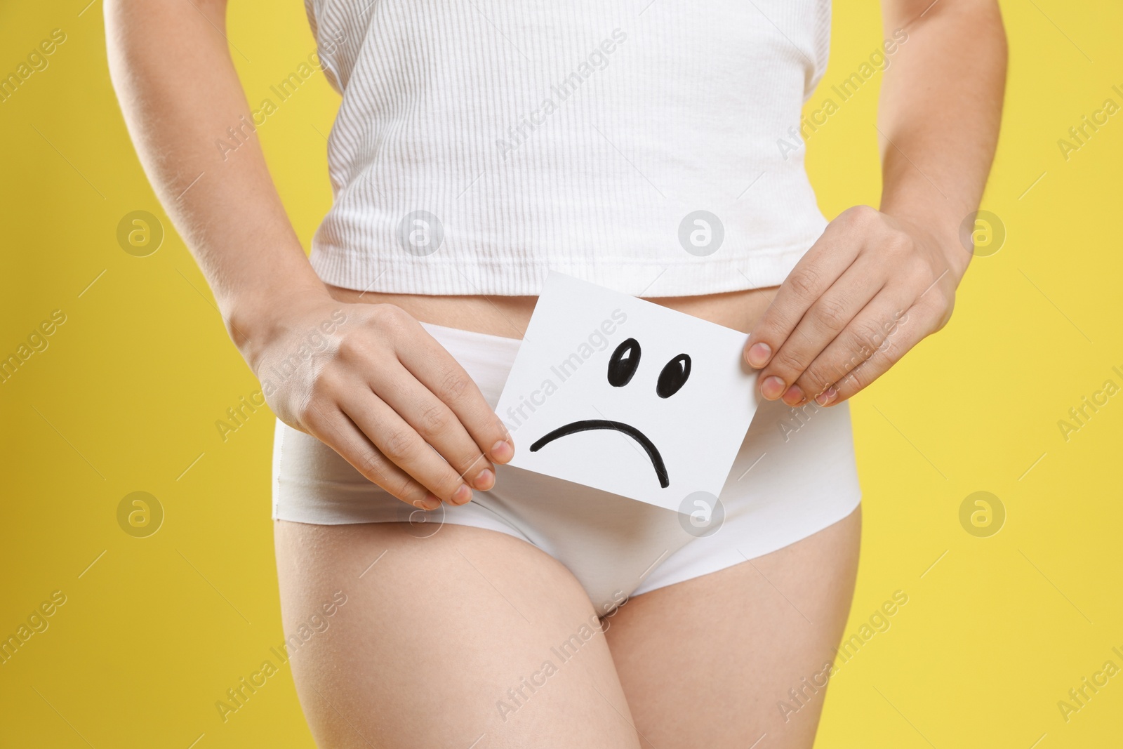 Photo of STD (sexually transmitted disease). Woman holding sticky note with drawn sad face on yellow background, closeup