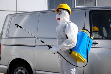 Photo of Pest control worker with spray tank near gray minibus outdoors