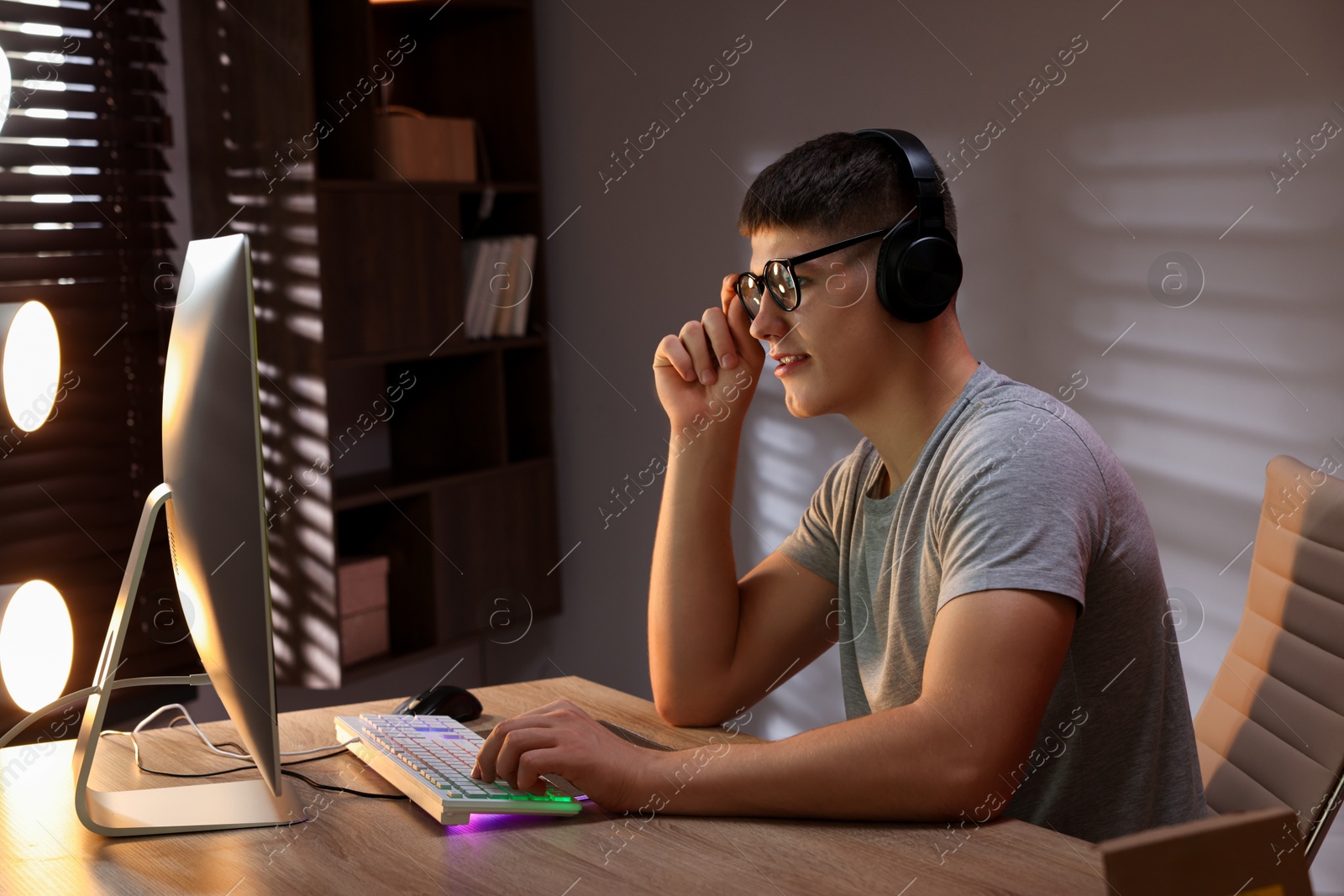 Photo of Young man playing video game with keyboard at wooden table indoors