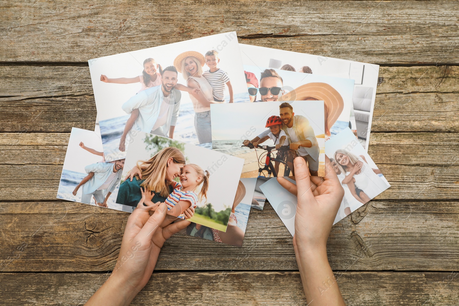 Photo of Woman with different photos in open photo album at wooden table, top view