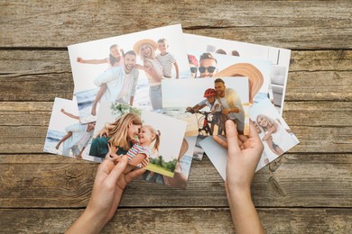 Photo of Woman with different photos in open photo album at wooden table, top view