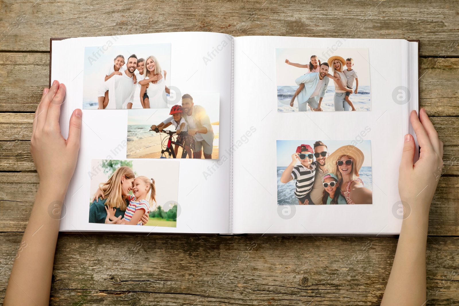 Photo of Woman with different photos in open photo album at wooden table, top view