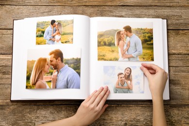 Photo of Woman with different photos in open photo album at wooden table, top view