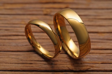 Photo of Beautiful golden wedding rings on wooden background, closeup