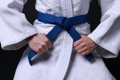 Photo of Karate fighter in kimono on black background, closeup