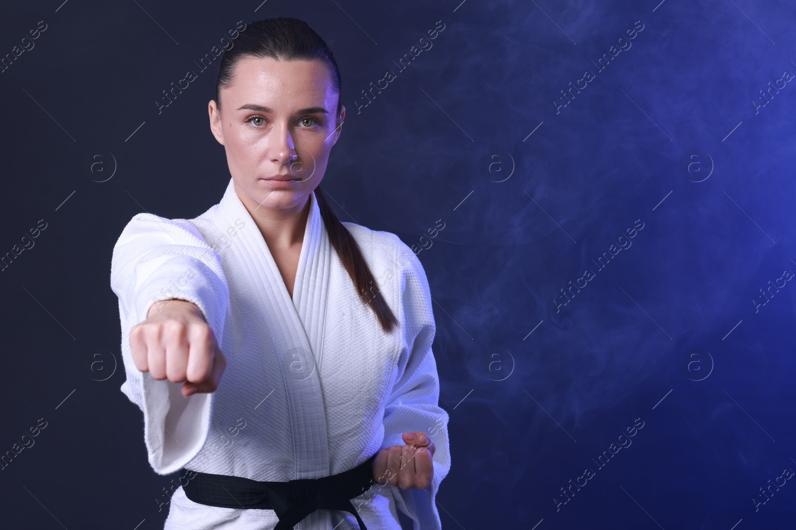 Photo of Karate fighter in kimono on dark blue background, space for text