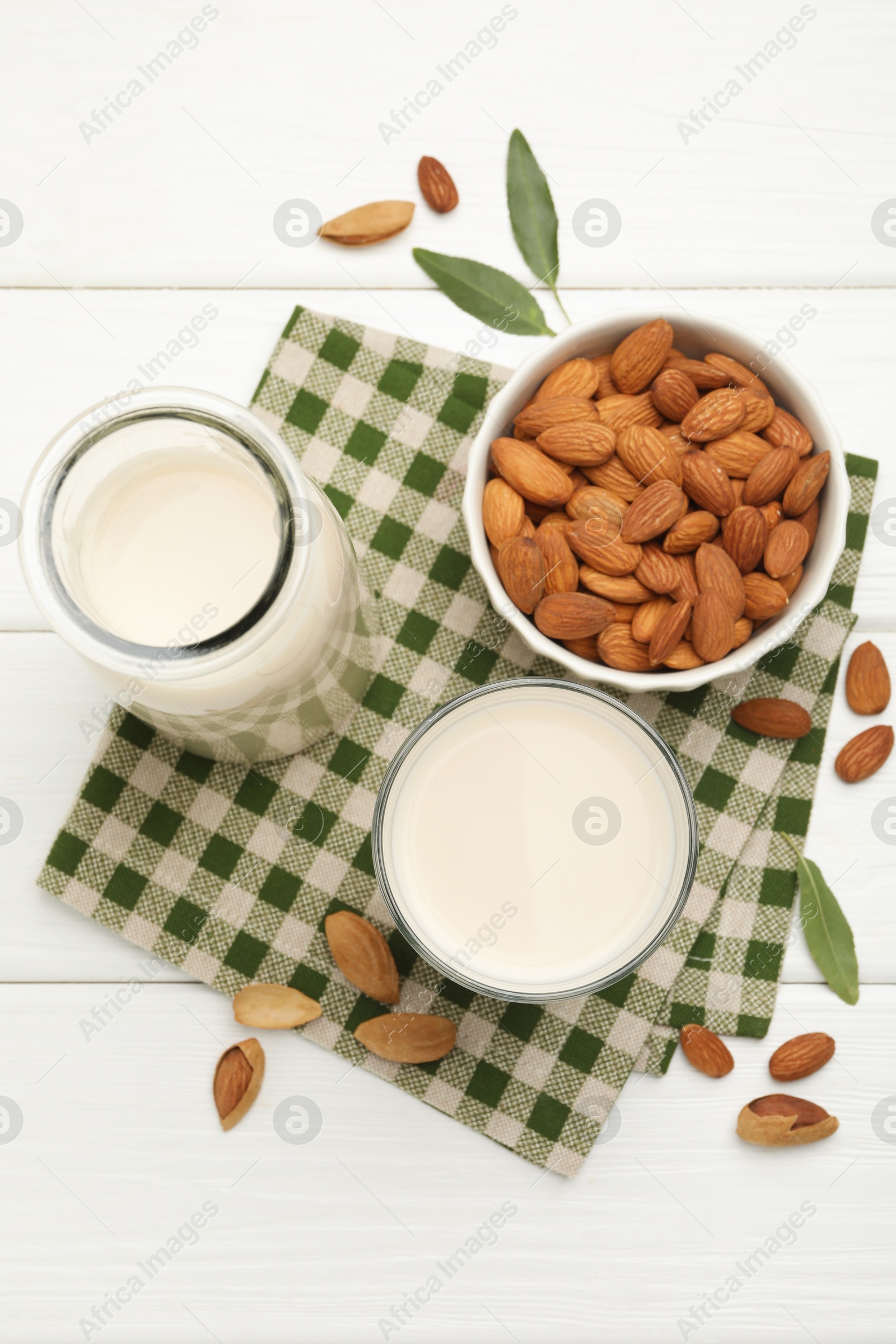 Photo of Fresh nut milk, almonds and green leaves on white wooden table, flat lay