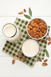 Photo of Fresh nut milk, almonds and green leaves on white wooden table, flat lay