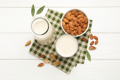 Fresh nut milk, almonds and green leaves on white wooden table, flat lay