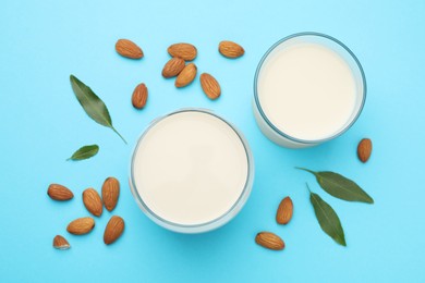 Photo of Fresh nut milk in glasses, almonds and green leaves on light blue background, flat lay