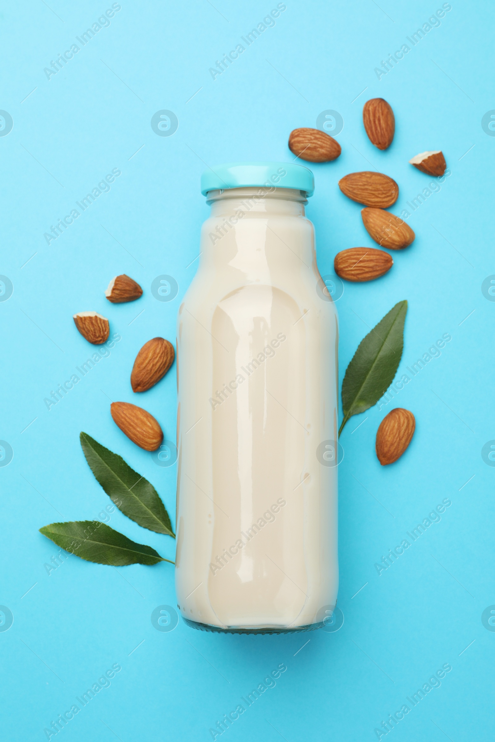 Photo of Fresh nut milk in glass bottle, almonds and green leaves on light blue background, top view