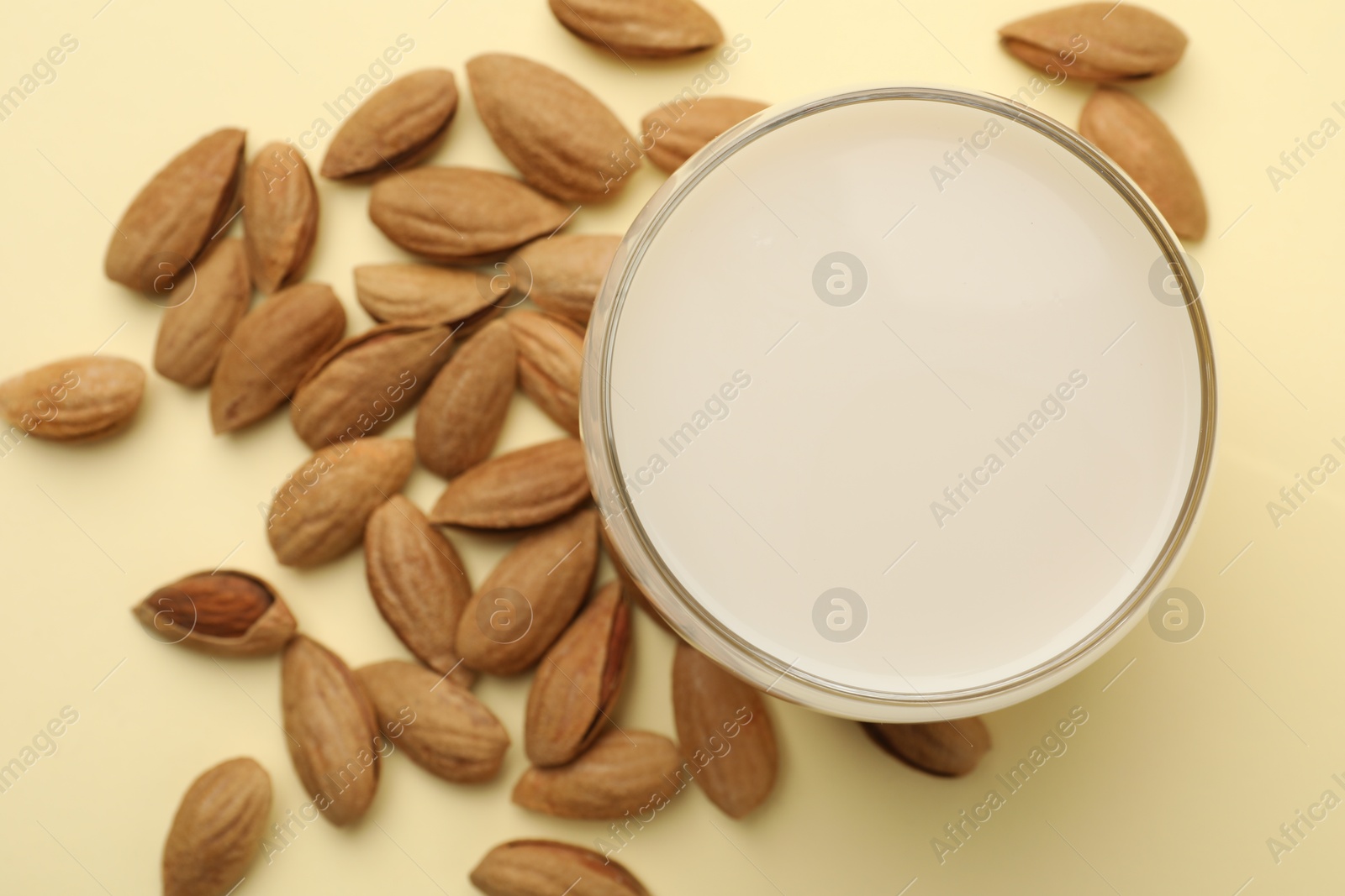 Photo of Fresh nut milk in glass and almonds on beige table, top view