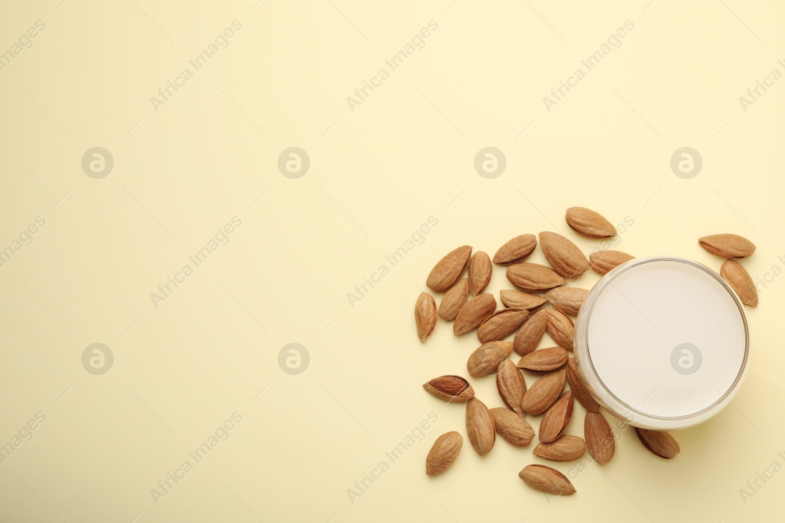 Photo of Fresh nut milk in glass and almonds on beige table, flat lay. Space for text