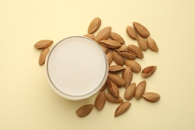 Photo of Fresh nut milk in glass and almonds on beige table, top view