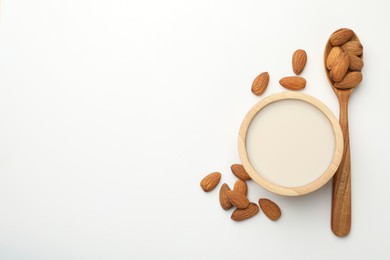 Fresh nut milk in bowl and almonds on white table, flat lay. Space for text