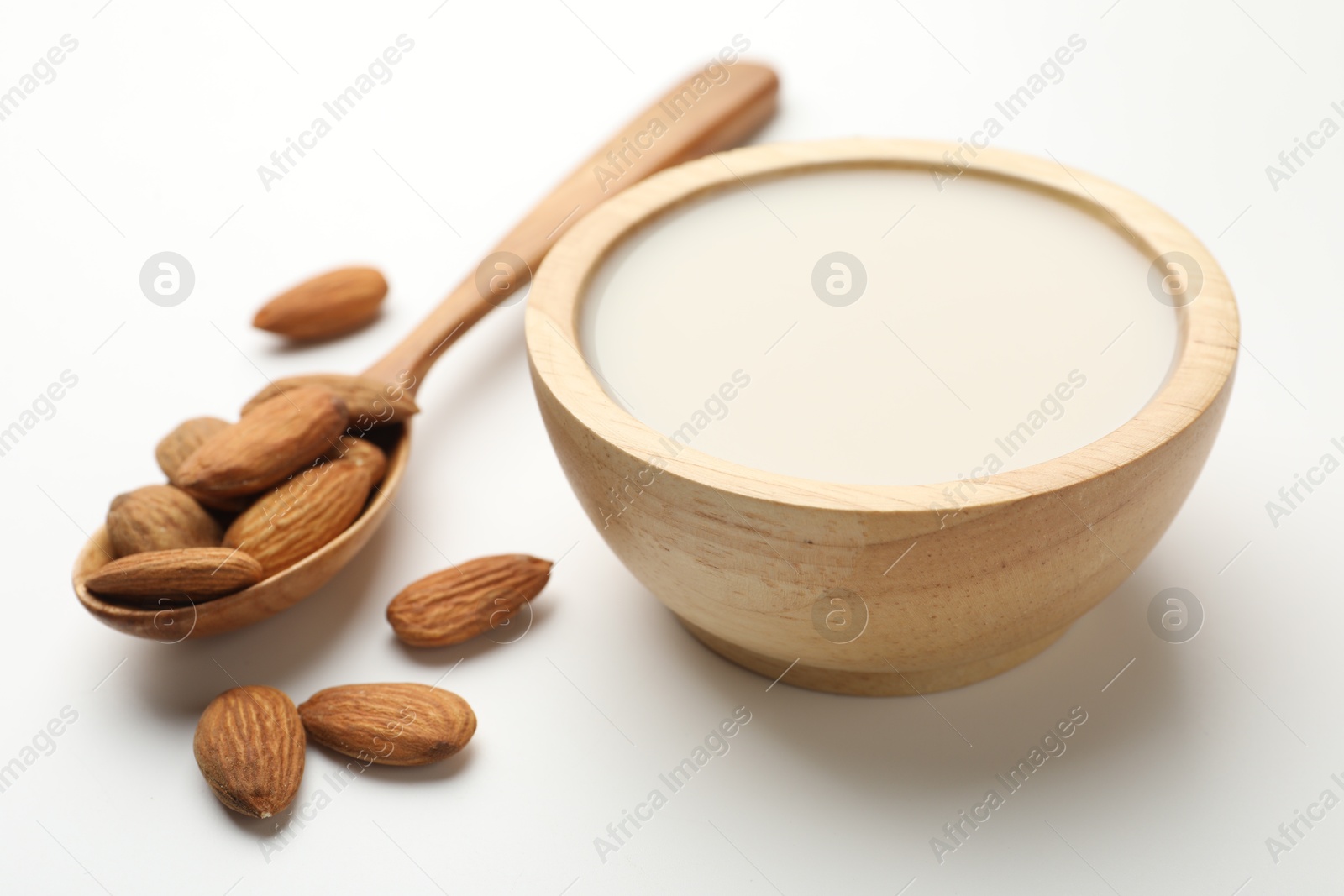 Photo of Fresh nut milk in bowl and almonds on white table, closeup