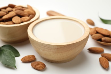 Fresh nut milk in bowl and almonds on white table, closeup