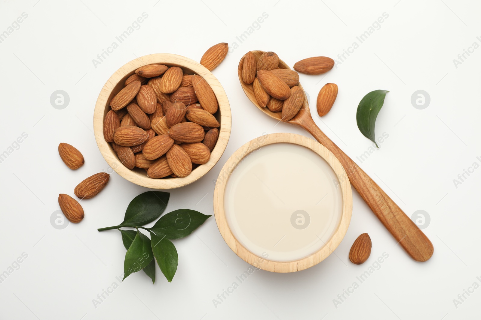 Photo of Fresh nut milk in bowl, almonds and green leaves on white table, flat lay