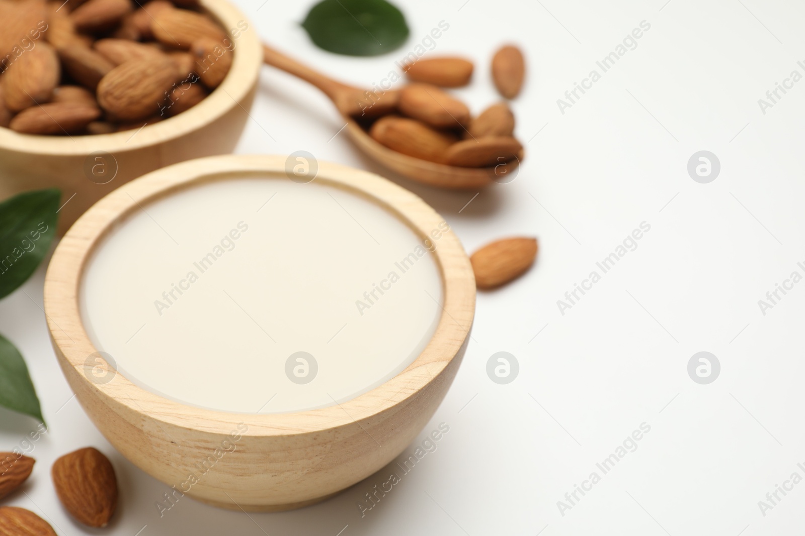 Photo of Fresh nut milk in bowl and almonds on white table, closeup. Space for text