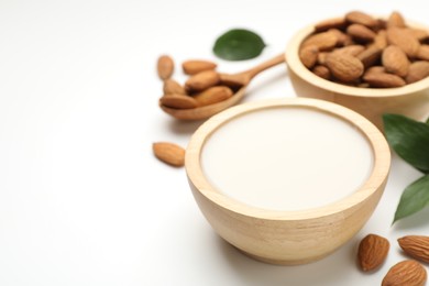 Fresh nut milk in bowl and almonds on white table, closeup. Space for text