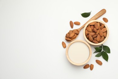 Fresh nut milk in bowl, almonds and green leaves on white table, flat lay. Space for text