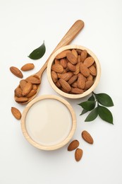 Fresh nut milk in bowl, almonds and green leaves on white table, flat lay