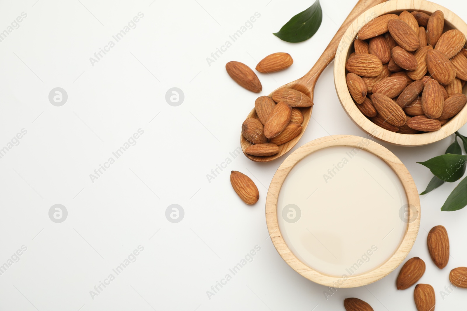 Photo of Fresh nut milk in bowl, almonds and green leaves on white table, flat lay. Space for text