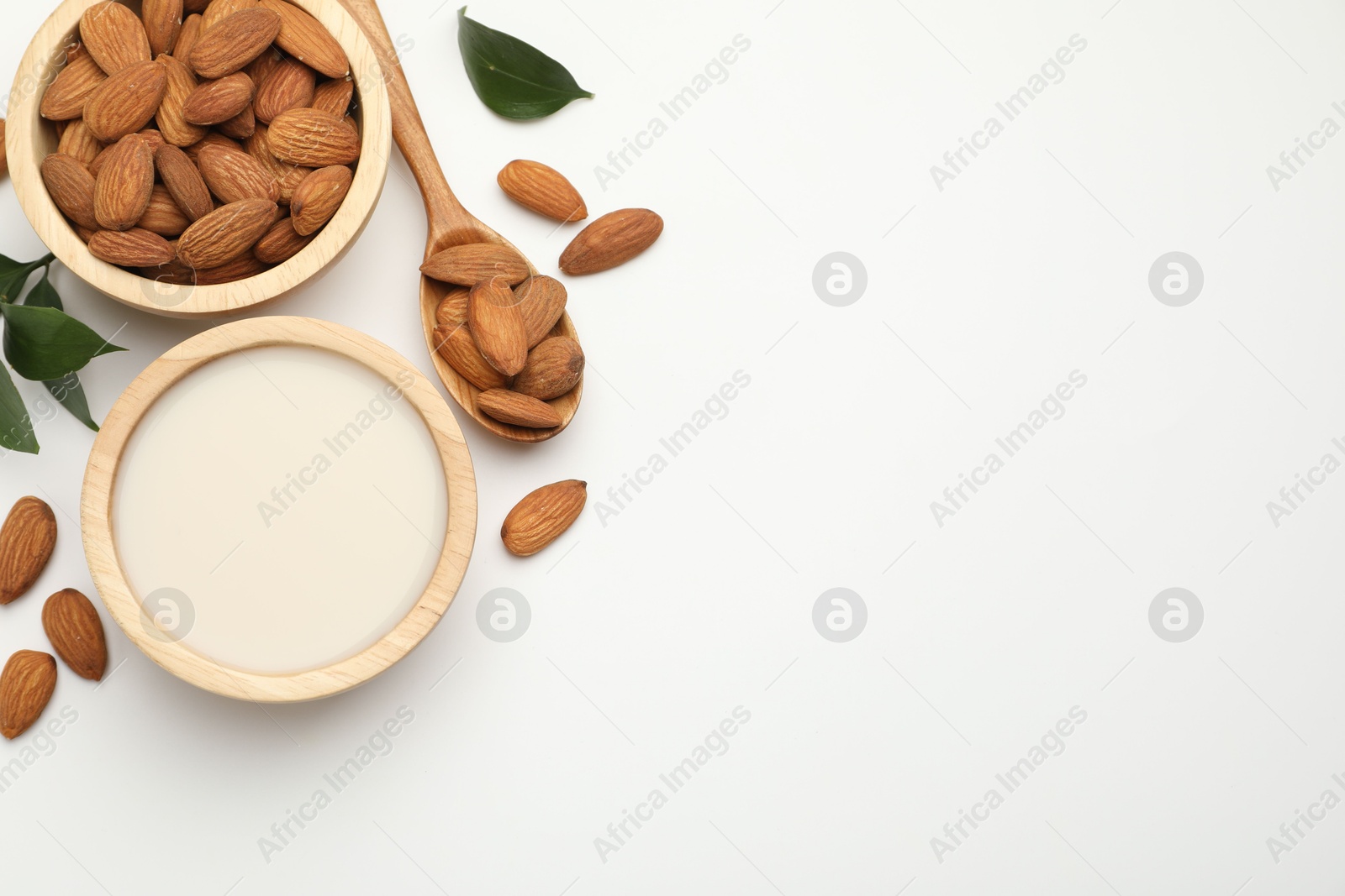 Photo of Fresh nut milk in bowl, almonds and green leaves on white table, flat lay. Space for text