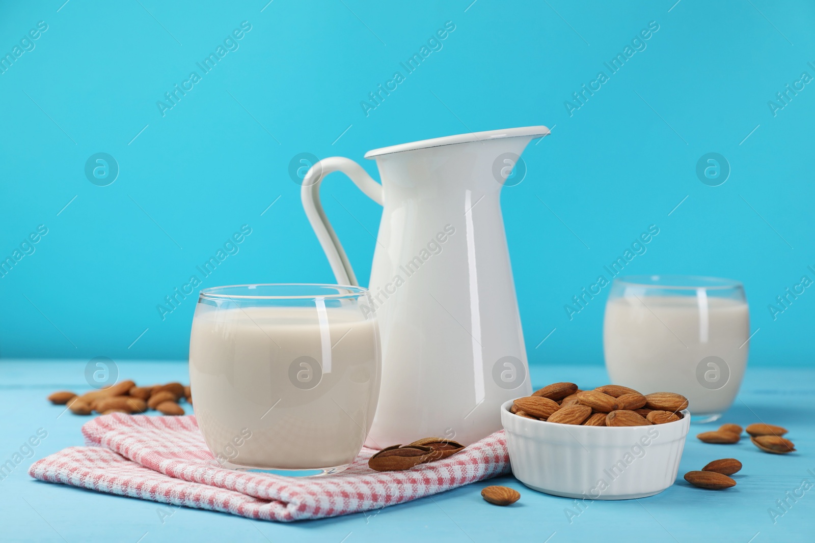 Photo of Fresh nut milk and almonds on light blue wooden table