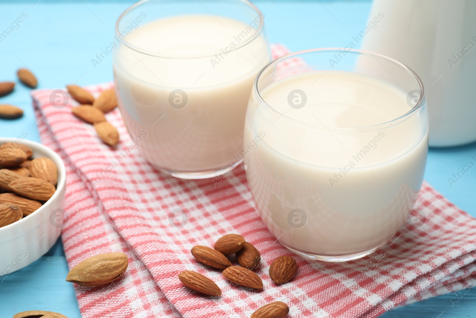 Photo of Fresh nut milk in glasses and almonds on light blue table, closeup