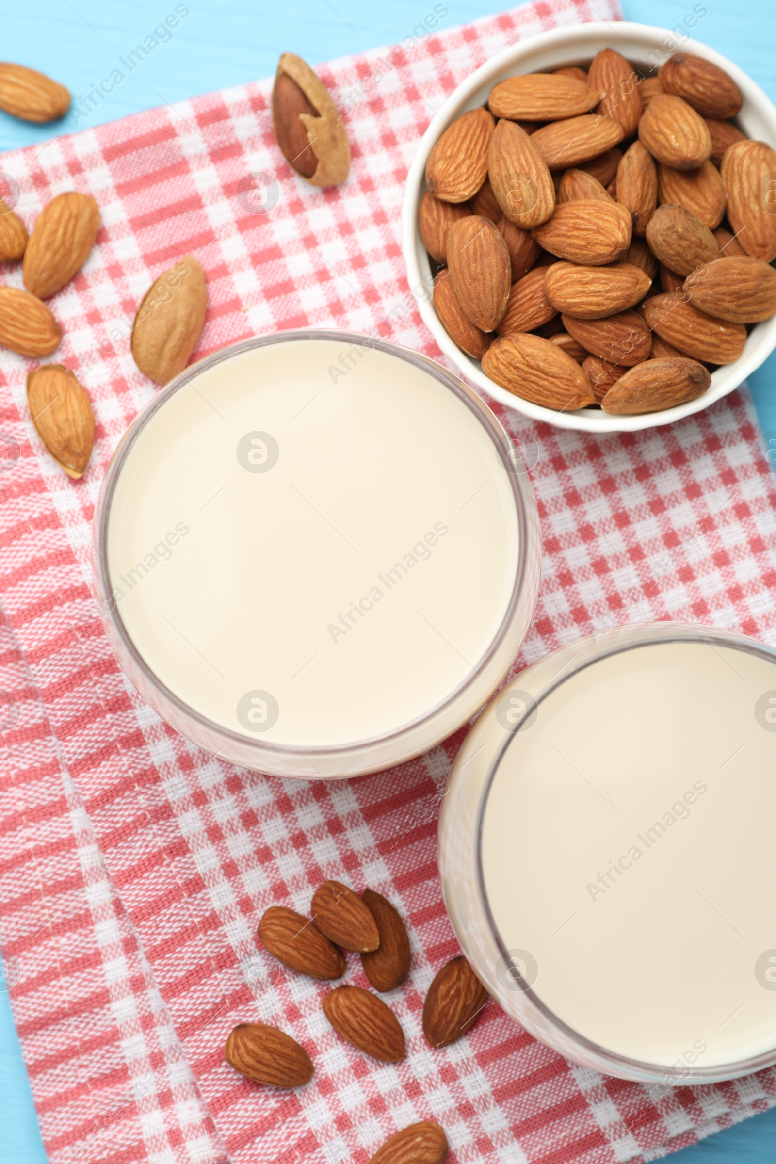 Photo of Fresh nut milk in glasses and almonds on light blue table, flat lay