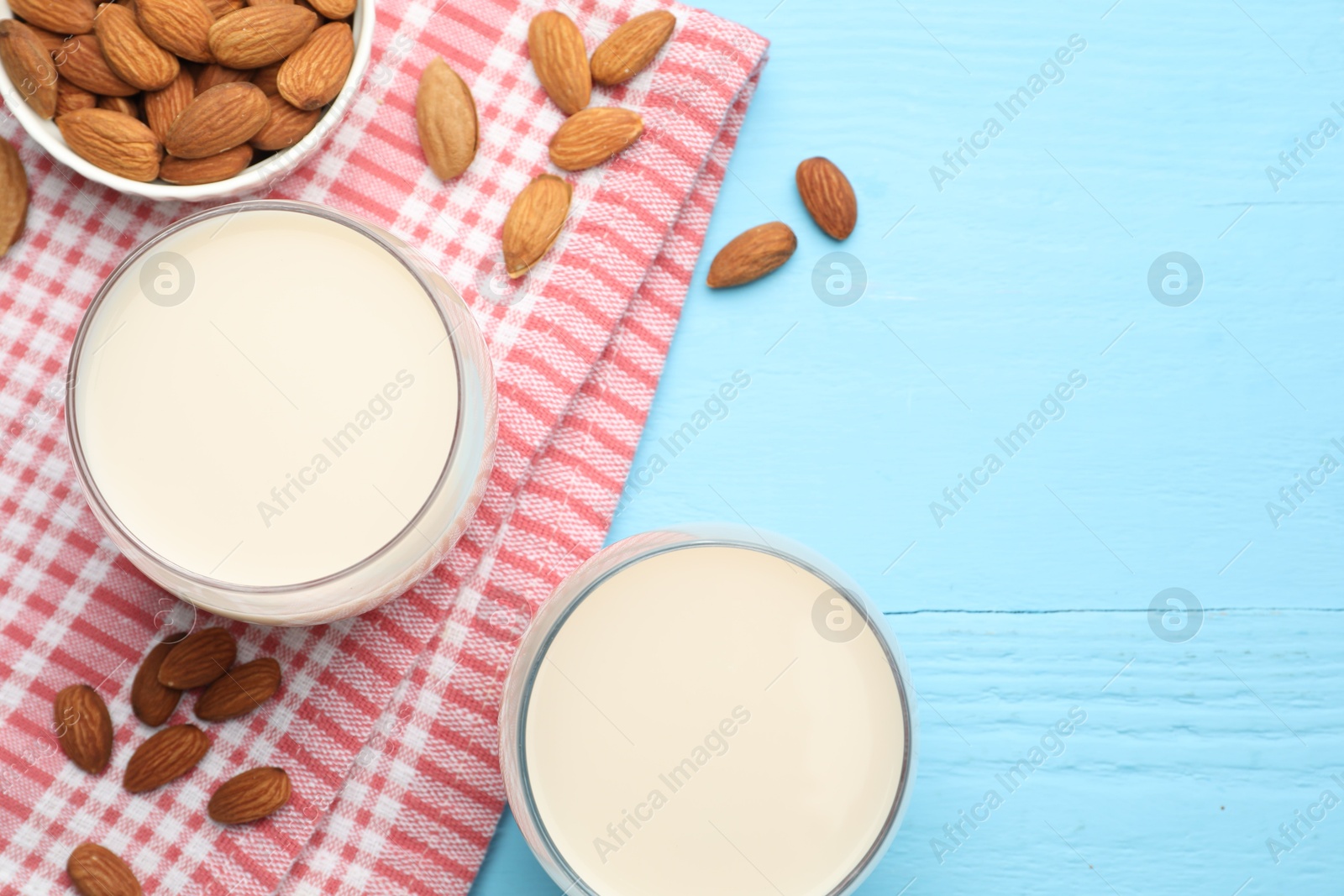 Photo of Fresh nut milk in glasses and almonds on light blue wooden table, flat lay. Space for text