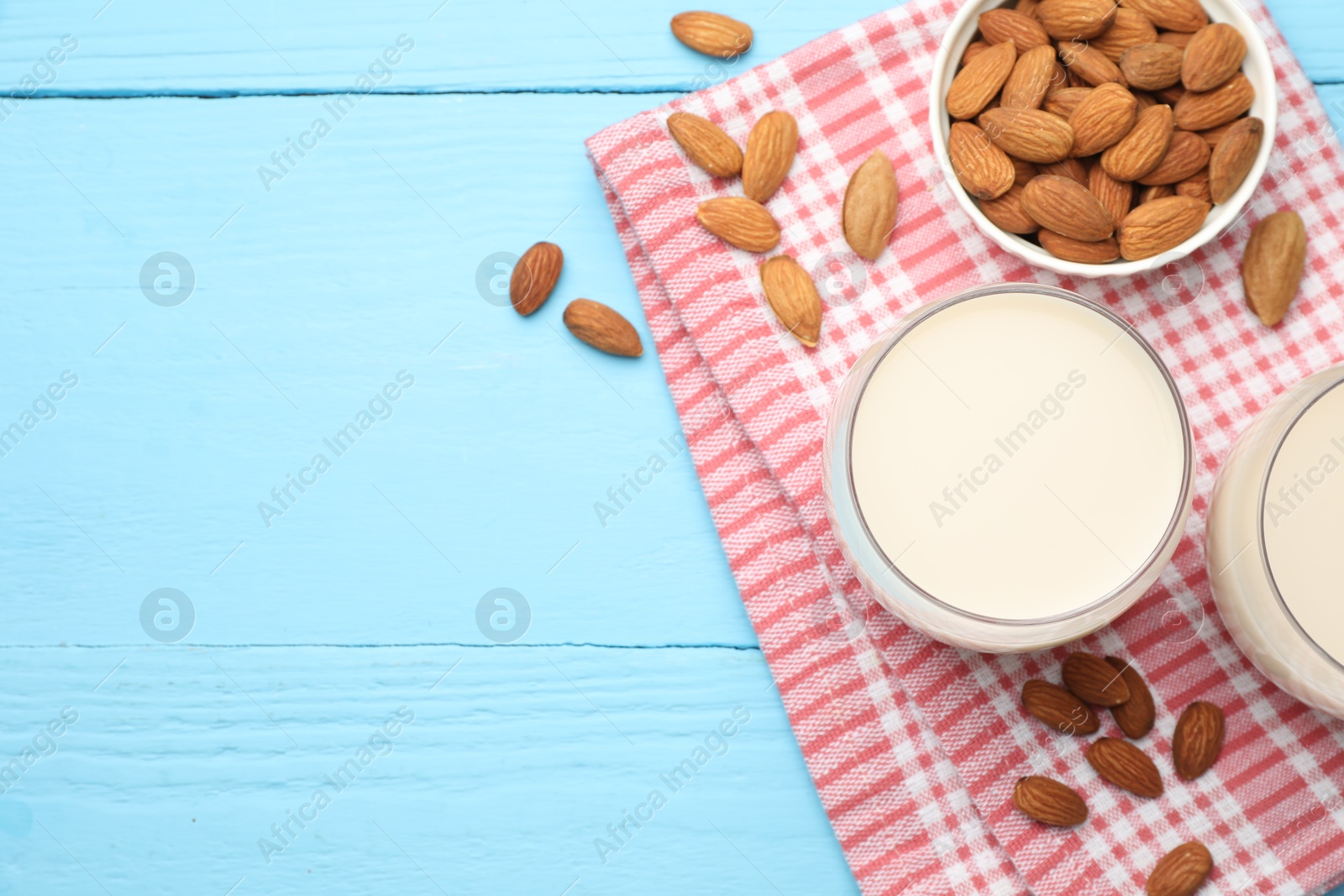 Photo of Fresh nut milk in glasses and almonds on light blue wooden table, flat lay. Space for text